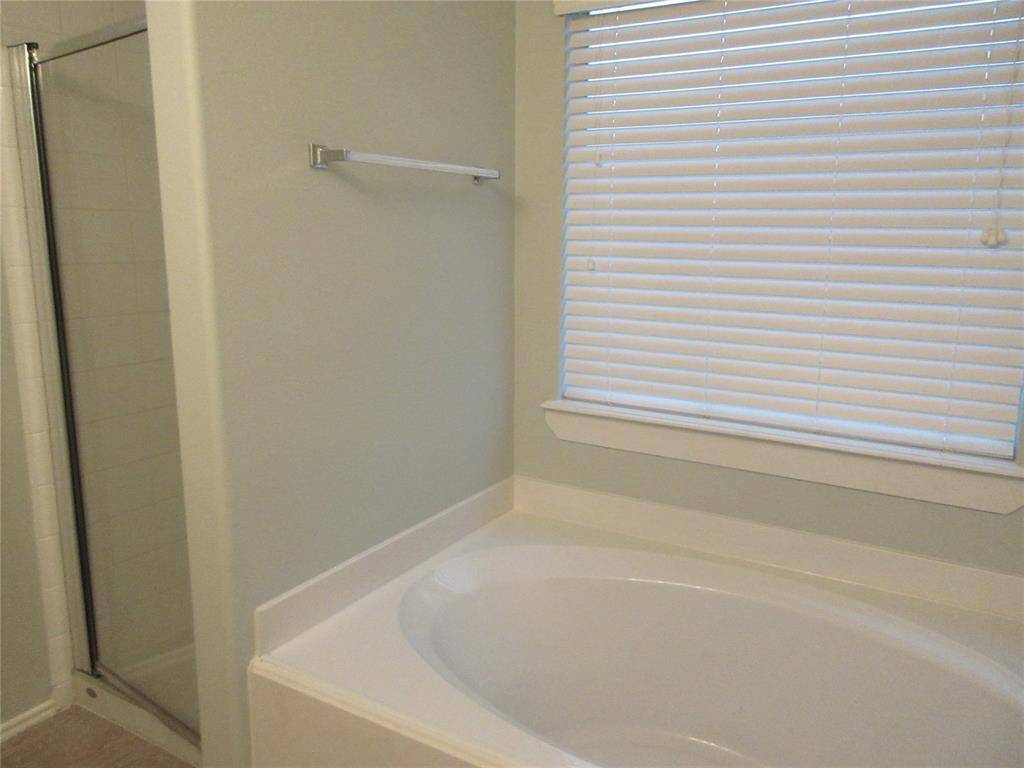 This bathroom features a spacious bathtub, a separate glass-enclosed shower, and a window with blinds for privacy. The neutral color scheme creates a clean and inviting atmosphere.