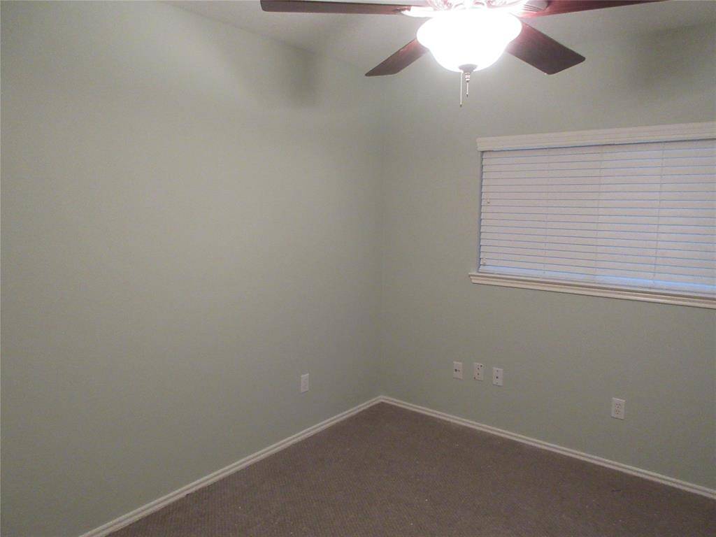 This room features soft green walls, a ceiling fan with light, carpeted flooring, and a window with blinds, creating a cozy and functional space.