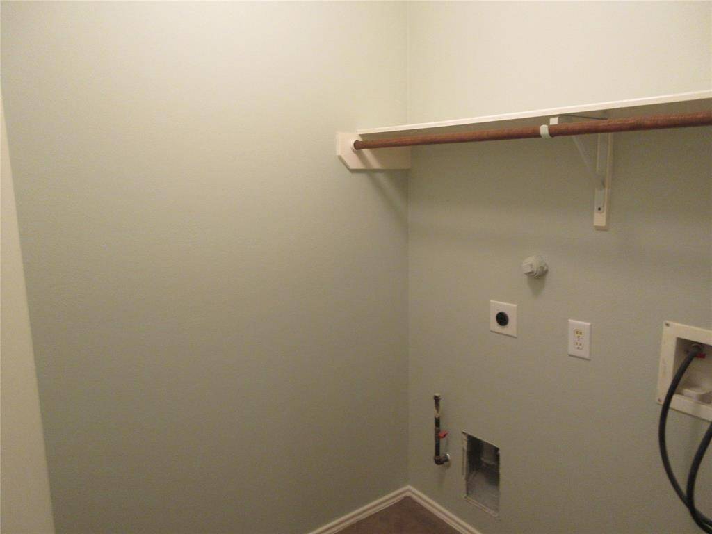 The utility room includes hookups for a washer and dryer. It features a light-painted wall, a wooden shelf with a hanging rod.
