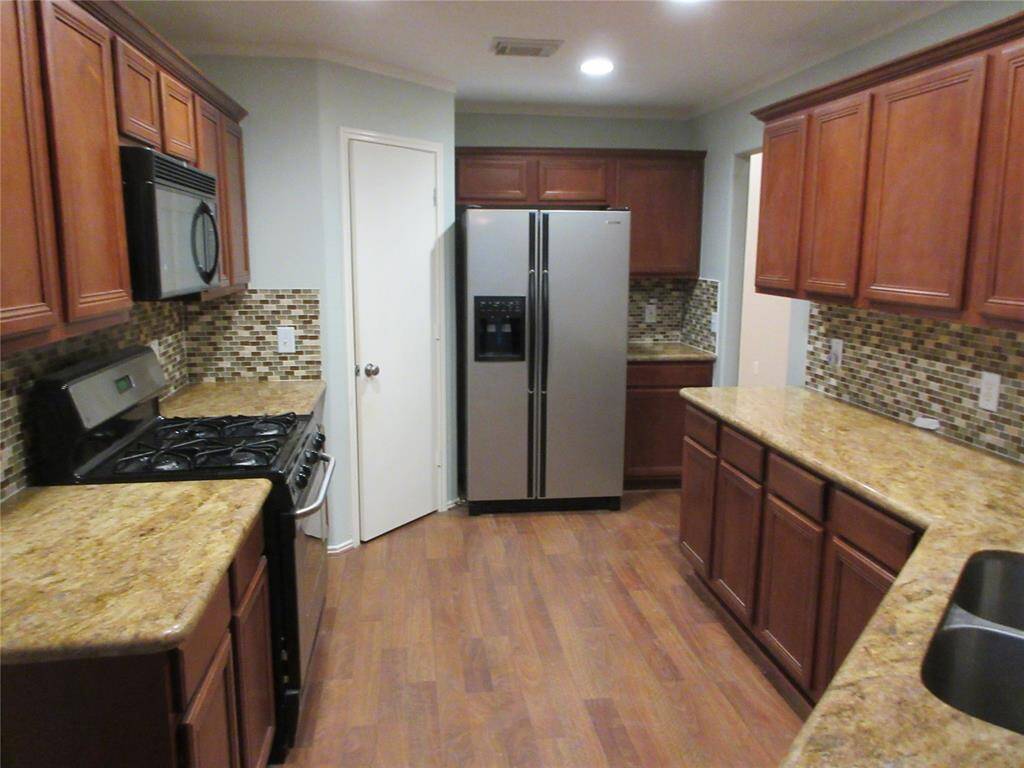 This kitchen features warm wood cabinetry and granite countertops, complemented by a tile backsplash. It includes stainless steel appliances and a double-door refrigerator. The layout is compact, with ample storage and counter space.