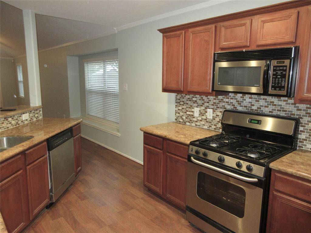 This kitchen features warm wood cabinetry, granite countertops, and a modern stainless steel fridge. The space is complemented by a stylish mosaic tile backsplash, providing a cozy and functional cooking area.