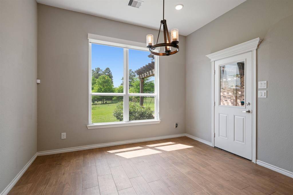 Charming breakfast area with large window overlooking lush green space and pergola-covered patio.