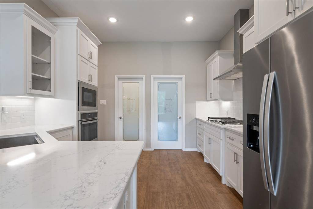 Chef's kitchen featuring quartz countertops, stainless appliances, dual pantries, and modern glass doors.