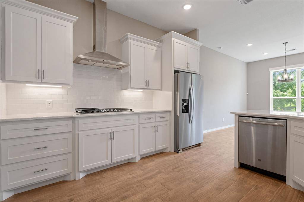 Crisp white cabinetry, subway tile backsplash, and vent hood elevate this gourmet kitchen space.