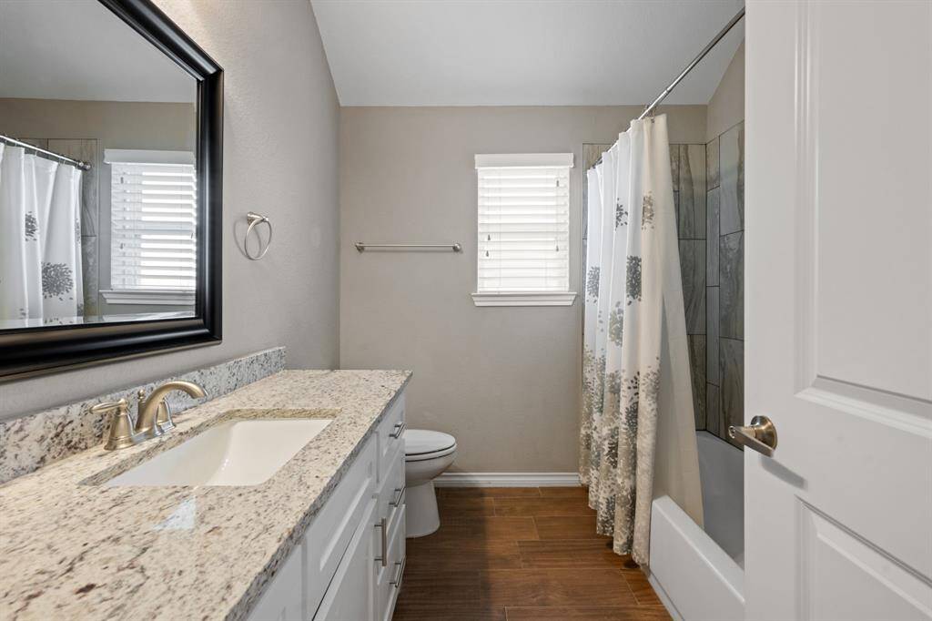 Sleek and stylish full bathroom with granite countertops, brushed nickel fixtures, and a large vanity mirror. Elegant wood-look tile flooring adds warmth.