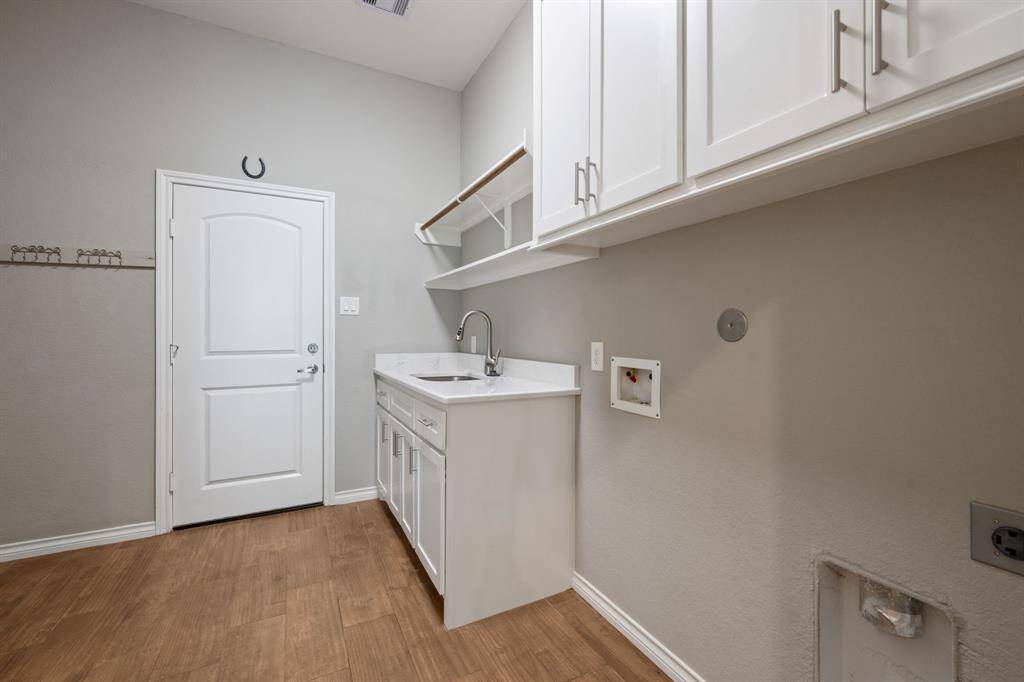 Oversized laundry room with built-in upper and lower cabinetry, utility sink, and hanging rod for added function and storage.