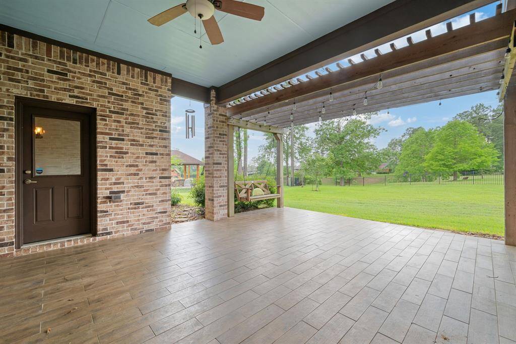 Expansive covered patio with wood-look tile flooring, a charming pergola, and ceiling fan—ideal for outdoor dining or entertaining.