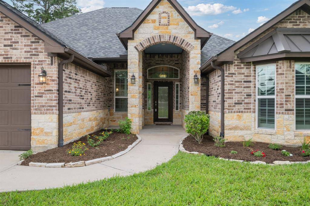 Covered front entry with stone archway, upgraded lighting, and lush flowerbeds offering a warm, elegant welcome.
