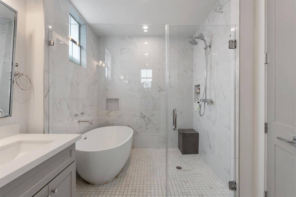 Unwind in the luxurious soaking tub set within a fully tiled wet room with a glass enclosure. The walk-in shower includes a built-in bench and a rainfall showerhead for a true spa experience.
