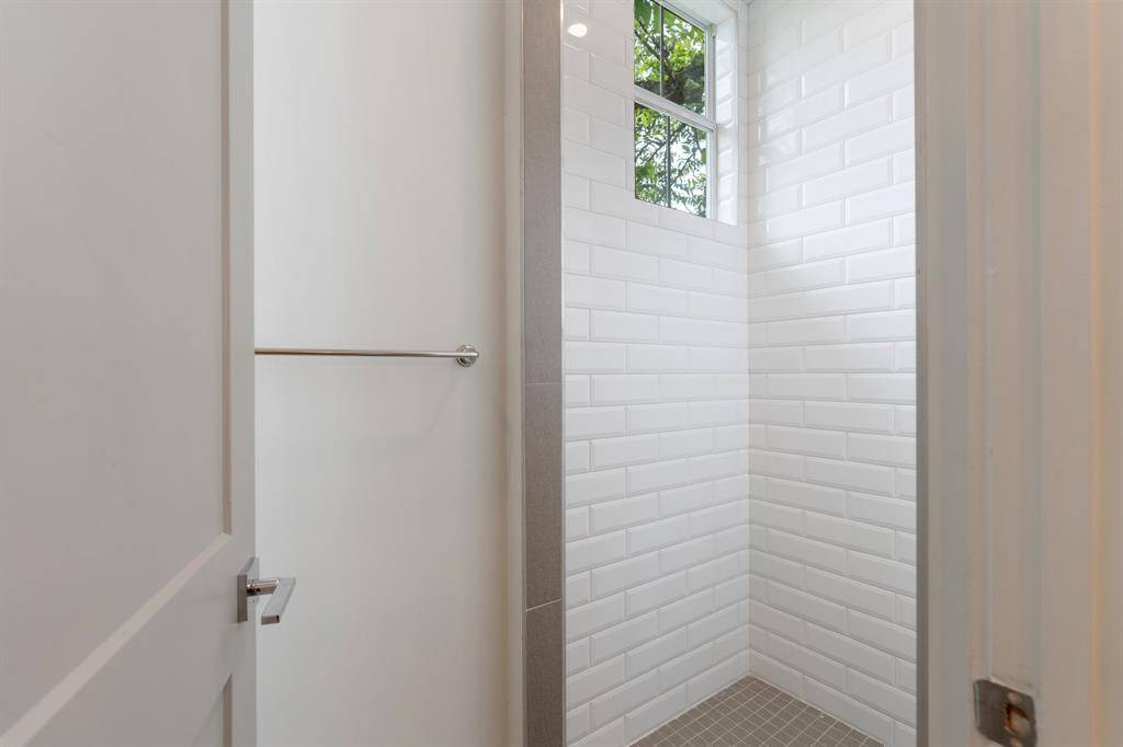 Crisp white tile and a window that frames outdoor greenery enhance the shower's airy, spa-like feel. This shower is part of a seamless layout connecting the secondary bedrooms.