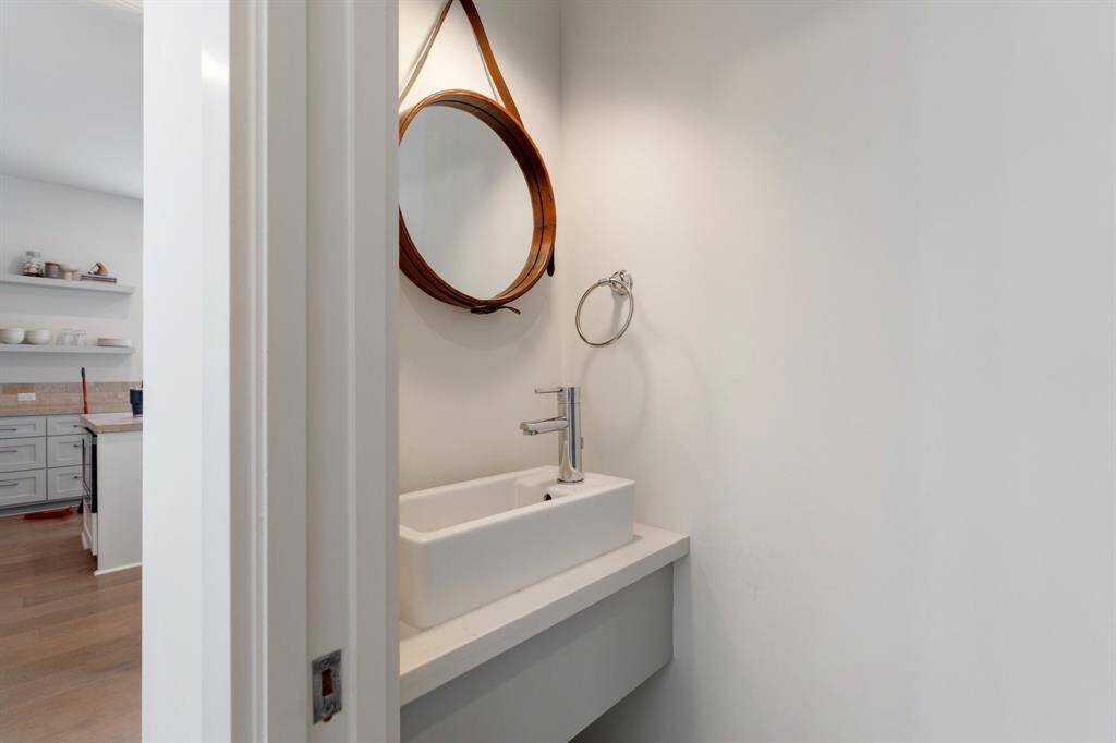 The stylish powder room is conveniently located off the main living area and features a modern vessel sink and a unique circular mirror. It offers guests a refined yet practical space.
