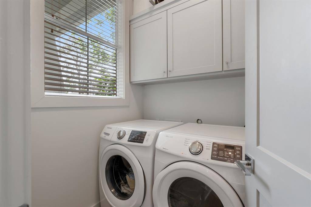 This laundry area includes front-load appliances, upper cabinetry for storage, and a window that fills the space with natural light. Efficient and tucked away, it enhances the home’s functionality.