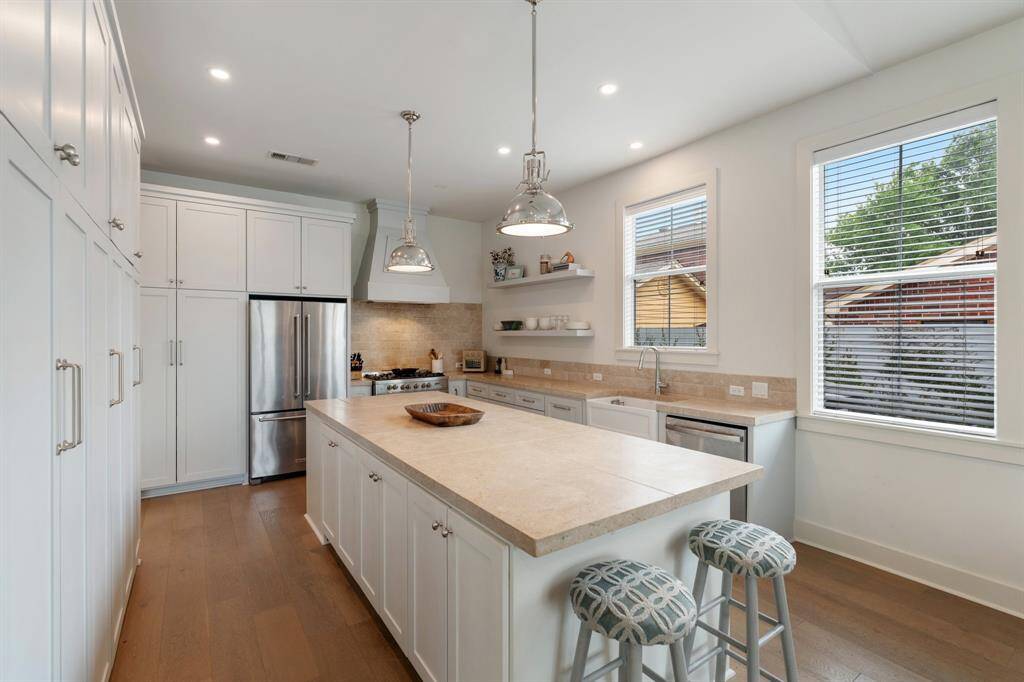 This angle highlights the spacious kitchen layout, from the generous island to the wall of cabinets offering maximum storage. The neutral palette complements the warm tones of the wood flooring.