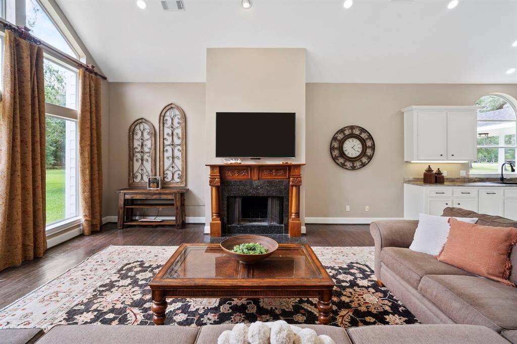 The room is bathed in natural light from expansive windows offering serene views of the lush greenery outside. High ceilings and tasteful lighting add elegance, while the layout is perfect for entertaining or family gatherings.