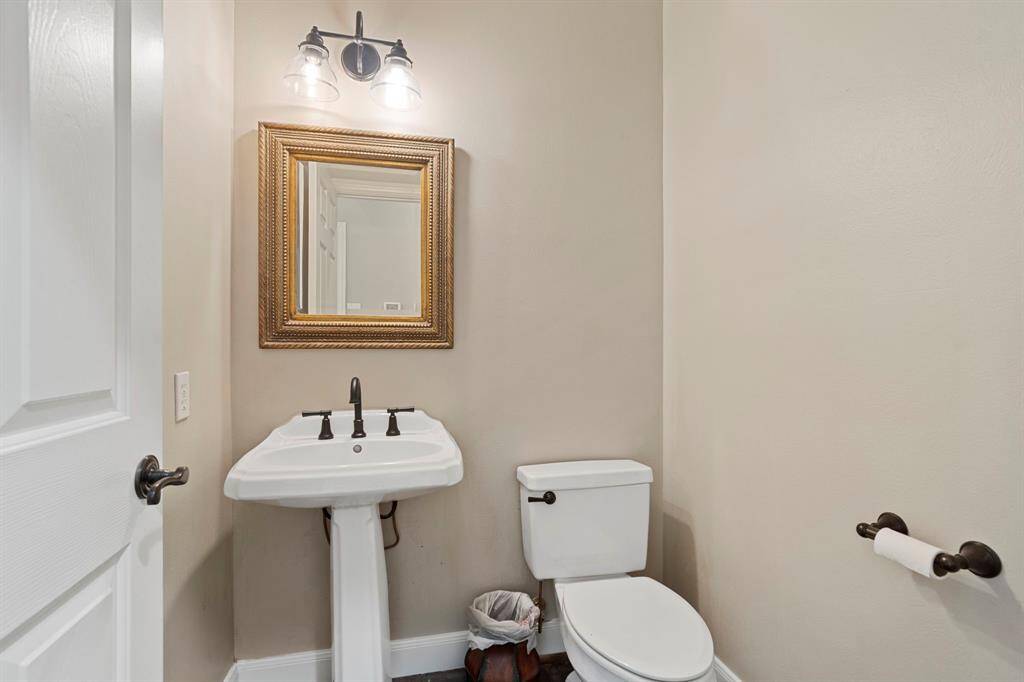 Featuring a sleek pedestal sink, modern fixtures, and a neutral color palette, the space is both functional and inviting. Its central location makes it easily accessible while maintaining privacy.