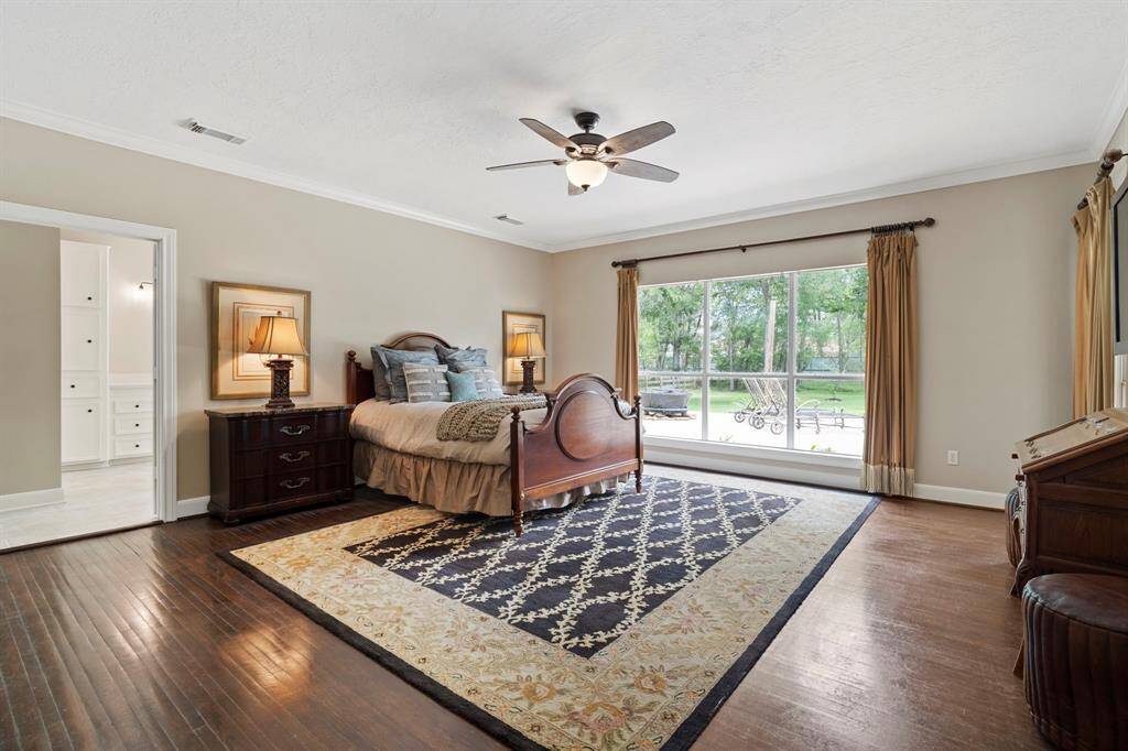 Spacious bedroom with hardwood floors and a large window offering a view of the backyard. Features a ceiling fan, elegant lighting, and ample natural light.