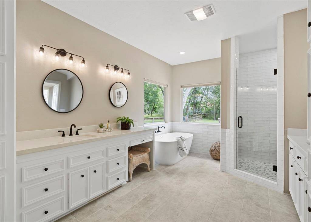 This spacious bathroom features a modern design with a freestanding tub, walk-in shower, dual sinks, and large windows offering plenty of natural light.