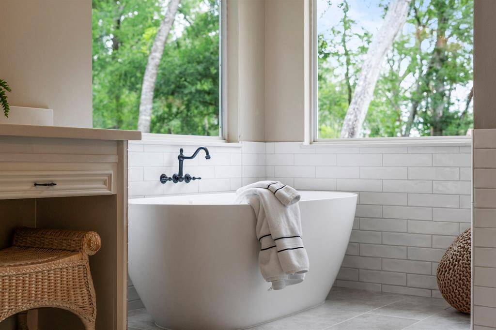Indulge in ultimate relaxation in the luxurious soaking tub, perfectly positioned to capture an abundance of natural light. Surrounded by oversized windows, this serene space offers a spa-like experience with tranquil views and a bright, airy ambiance