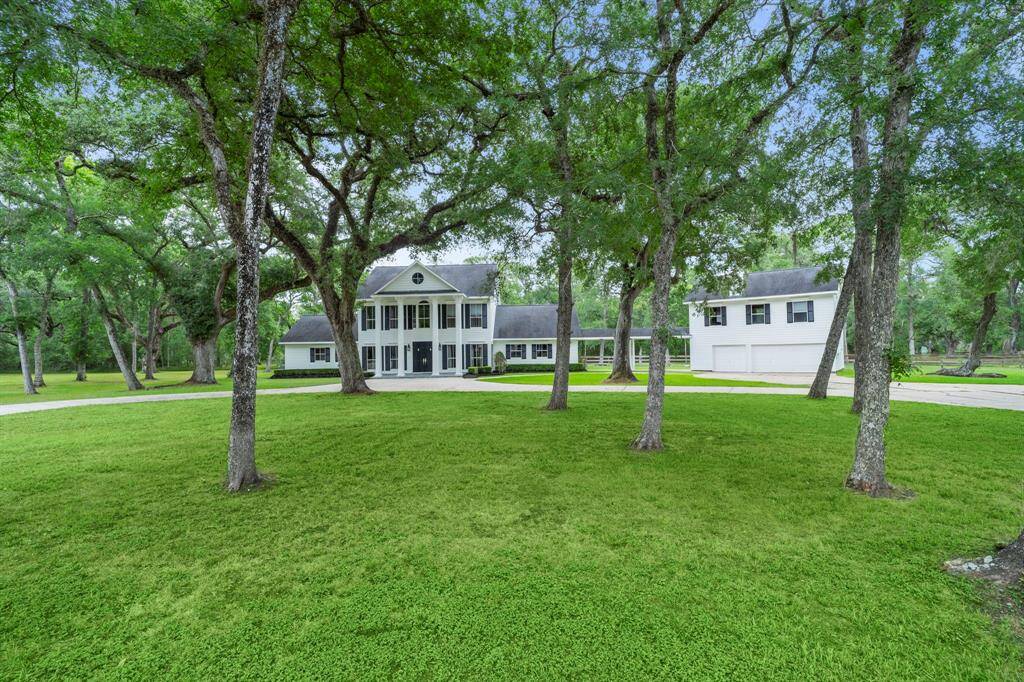 A grand two-story colonial-style home with elegant columns and a symmetrical facade. The house is surrounded by lush greenery and has a spacious driveway, offering a serene and inviting atmosphere.