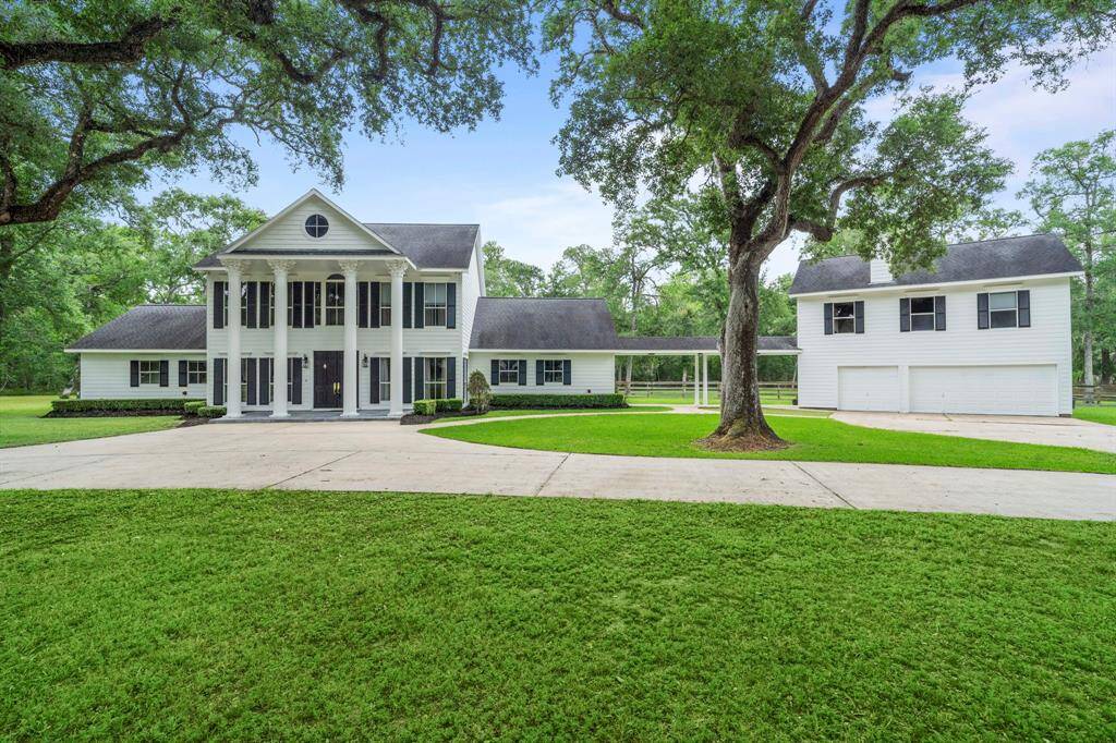 This elegant two-story home features a classic colonial design with tall columns, a large front porch, and expansive windows. It’s set on a spacious and well-maintained lawn with mature trees.
