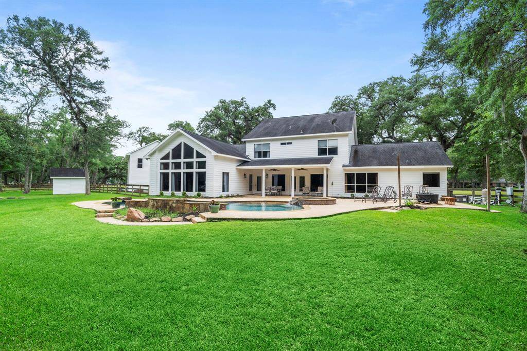 The backyard features a pool, patio area, and lush green lawn, surrounded by mature trees, offering plenty of outdoor space and privacy.