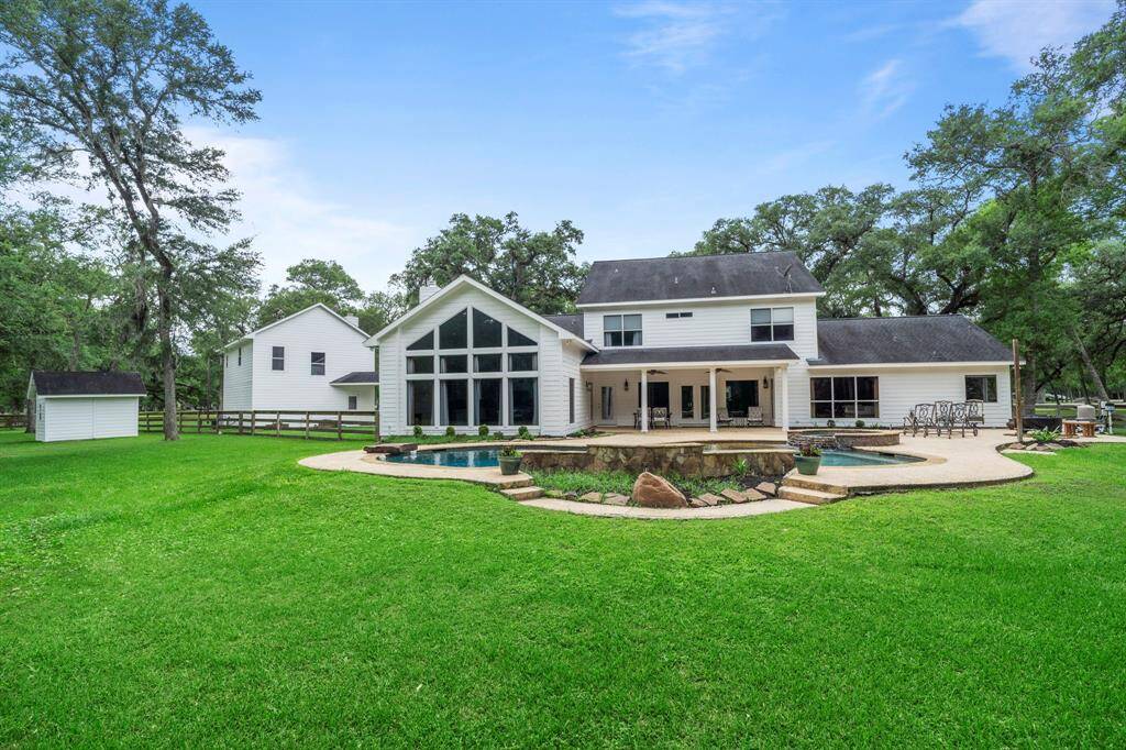 This home features a beautifully landscaped yard with a small pool and stone patio, set against a backdrop of lush greenery and mature trees, offering a serene and inviting atmosphere.