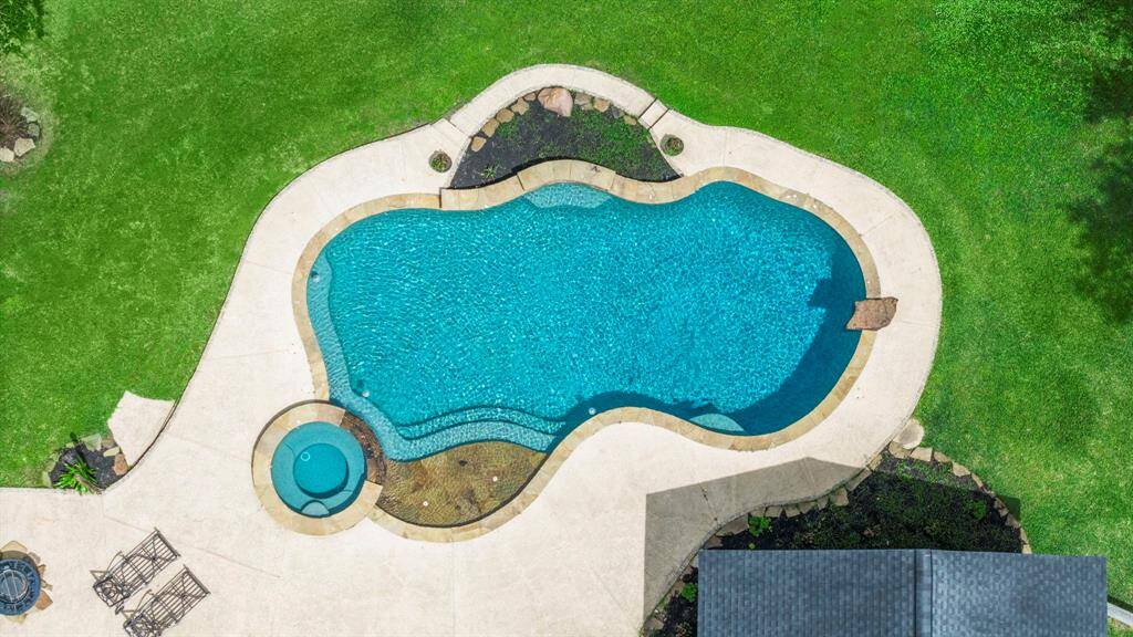 Beautifully landscaped backyard featuring a freeform swimming pool with an attached spa. The pool area is surrounded by lush green grass and a spacious patio, ideal for outdoor entertaining.