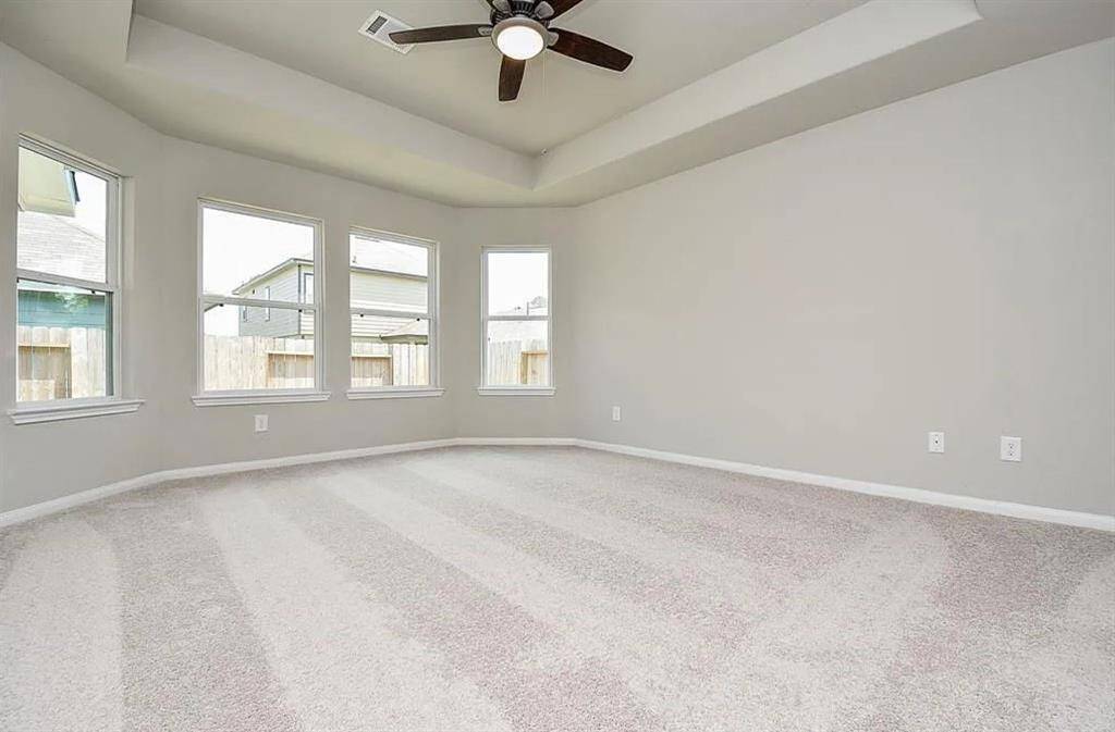 Spacious primary bedroom with tray coffered ceilings, plush carpeting, and abundant natural light.
