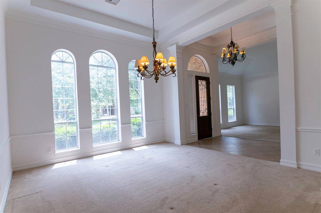 This spacious room features large arched windows that let in plenty of natural light, elegant chandeliers, and a welcoming entryway with a decorative glass door.