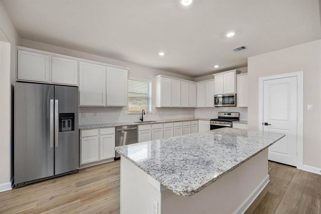 Step into this beautifully designed kitchen boasting a spacious island with a large breakfast bar overlooking the living room, a chic herringbone pattern backsplash, and modern stainless steel appliances. Perfect for entertaining and everyday living!