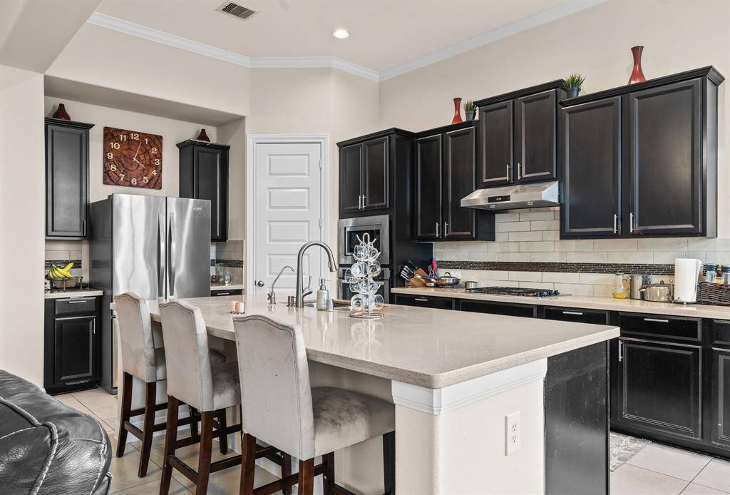 This modern kitchen features sleek dark cabinetry, stainless steel appliances, and a large island with seating for four. The light countertops and backsplash create a bright, inviting space perfect for cooking and entertaining.
