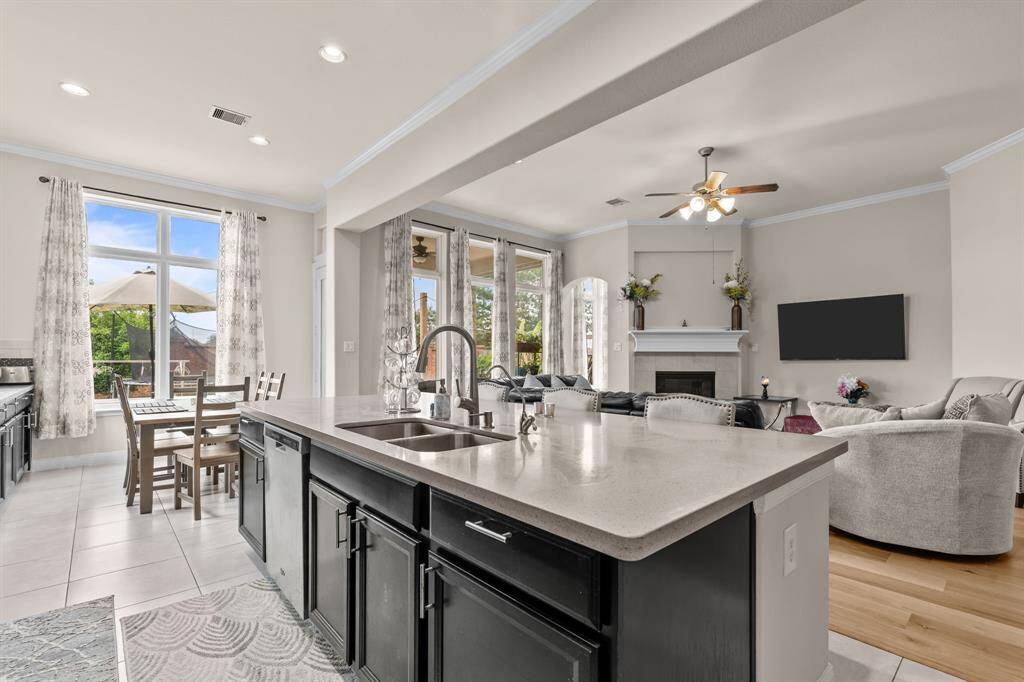 This open-concept living space features a modern kitchen with a large island and sleek countertops, flowing into a cozy living area with a fireplace and ample natural light from large windows and glass doors. Ideal for entertaining, it combines functionality with style.
