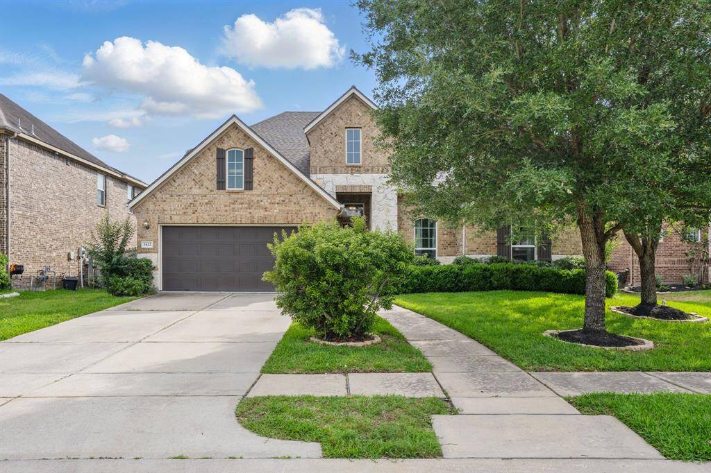 This is a charming two-story brick home featuring a two-car garage, a well-maintained front yard with lush greenery, and a walkway leading to the entrance. It's situated in a suburban neighborhood with a pleasant, inviting curb appeal.