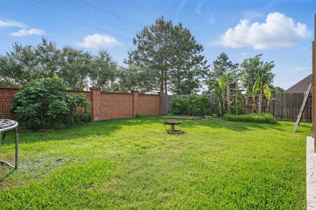 Spacious backyard with lush green grass, bordered by a red brick wall and wooden fence. Features mature trees and plants, offering privacy and a serene atmosphere. Ideal for outdoor activities and relaxation.