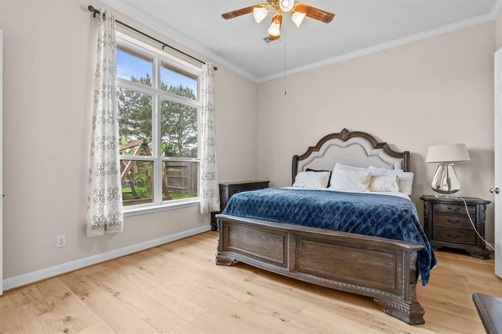 This cozy bedroom features a large window allowing natural light to brighten the space. It includes a comfortable bed with a stylish headboard, hardwood floors, and a ceiling fan. The neutral walls create a warm and inviting atmosphere.