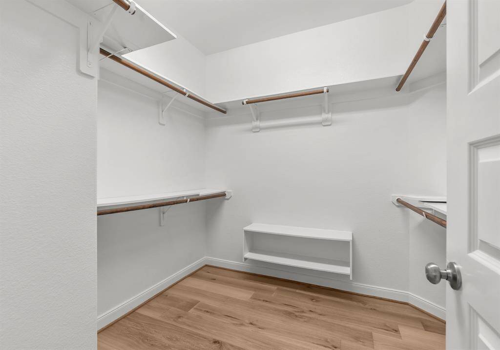 Spacious walk-in closet with wooden floors, multiple shelves, and hanging rods, offering ample storage.
