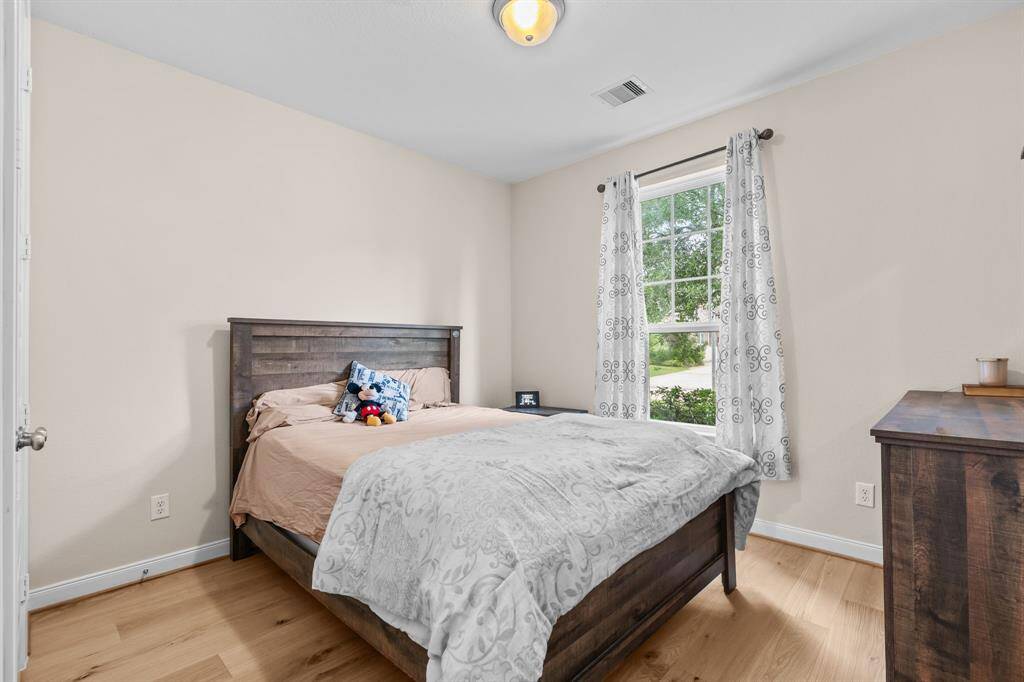 This bedroom features hardwood floors and a window lets in natural light, creating a warm and inviting atmosphere.