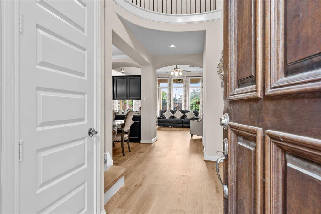 This inviting entryway features a wooden door leading into a bright, open-concept living space with light wood flooring. The area flows into a dining room with dark cabinetry and a cozy living room with large windows that let in natural light.