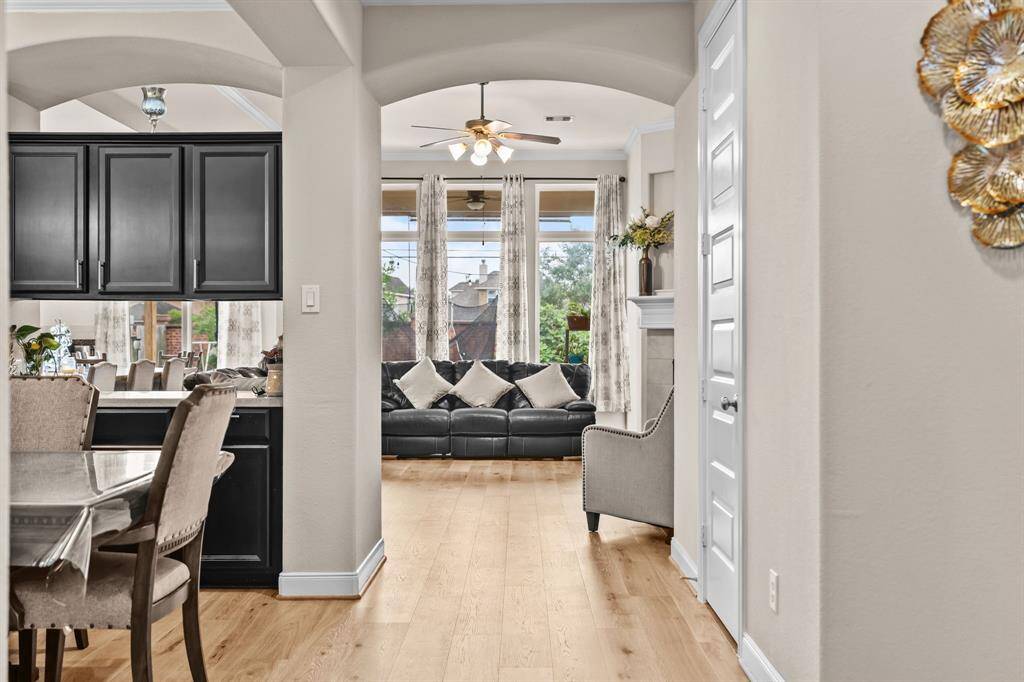 Open concept living area with hardwood floors. It features a cozy seating area by large windows, allowing natural light to flood the space. The dining area is adjacent, with a modern kitchen featuring dark cabinetry. Elegant decor and neutral tones create a welcoming atmosphere.