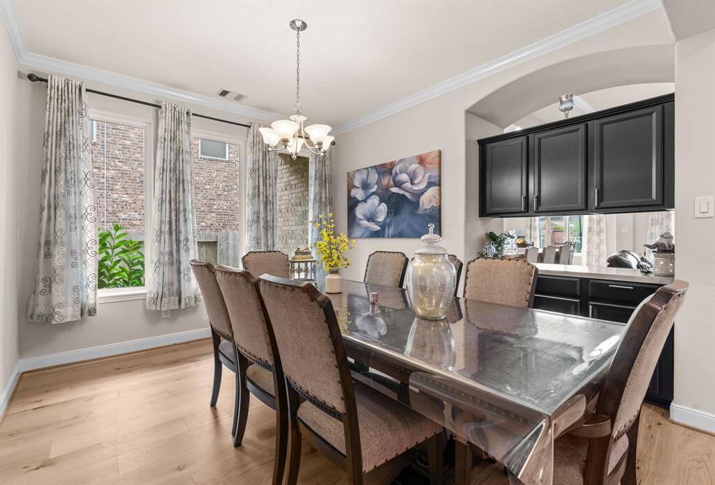 Bright dining area with large windows, elegant chandelier. Features hardwood floors, dark cabinetry creating a warm, inviting space.