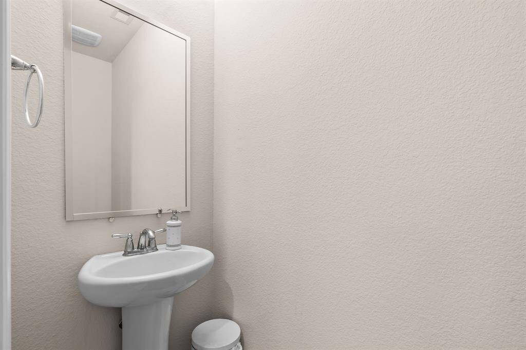 This is a compact, modern half-bathroom featuring a pedestal sink, a large mirror, and neutral-colored walls, ideal for guest use.