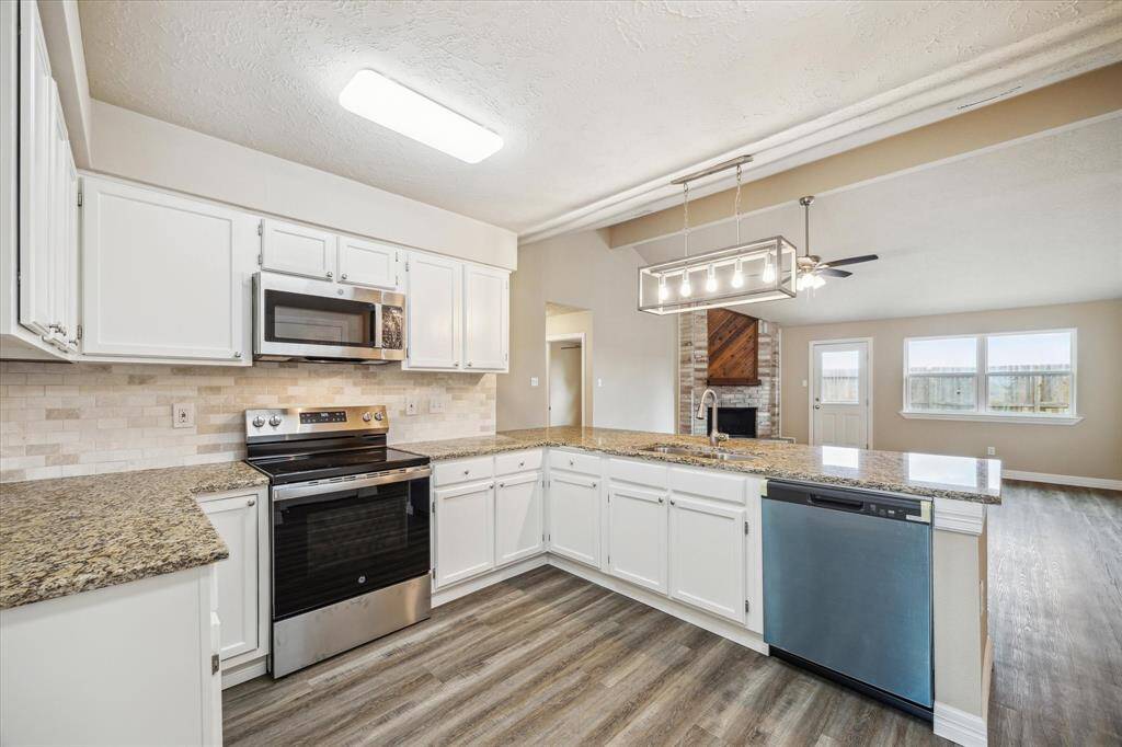 This kitchen features modern appliances, granite countertops, and white cabinetry. It opens to a spacious living area with large windows - creating a bright and inviting atmosphere.