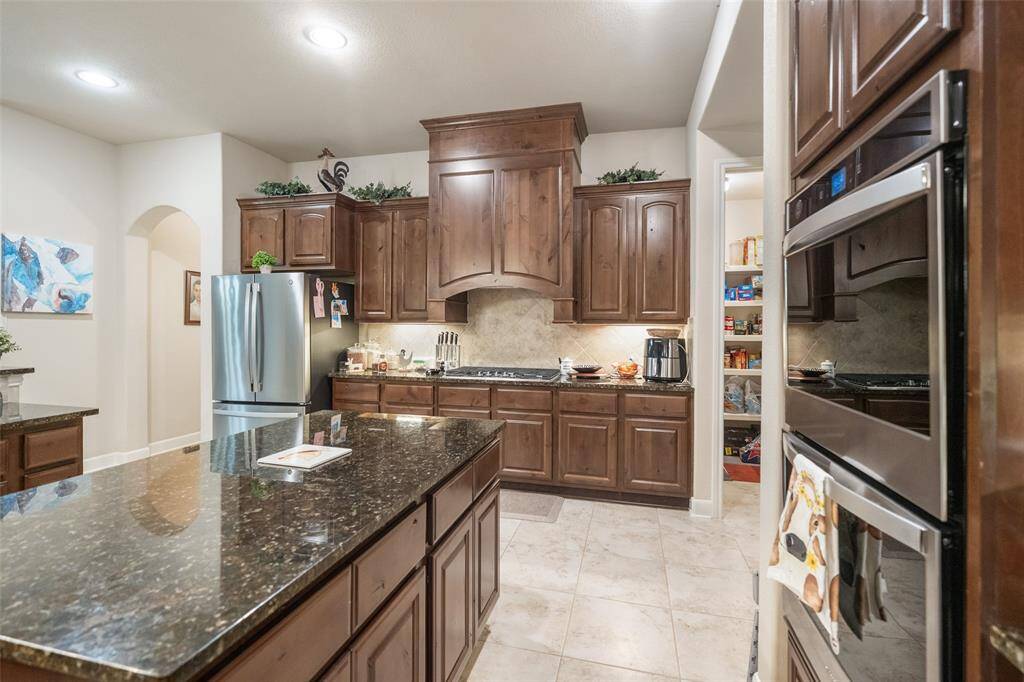 Ditch the takeout and enjoy home-cooked meals in this spacious kitchen featuring stainless steel appliances, a center island, and a wraparound bar perfect for casual dining. Rich wood cabinetry with oversized drawers and a walk-in pantry make it easy to keep everything organized and within reach.