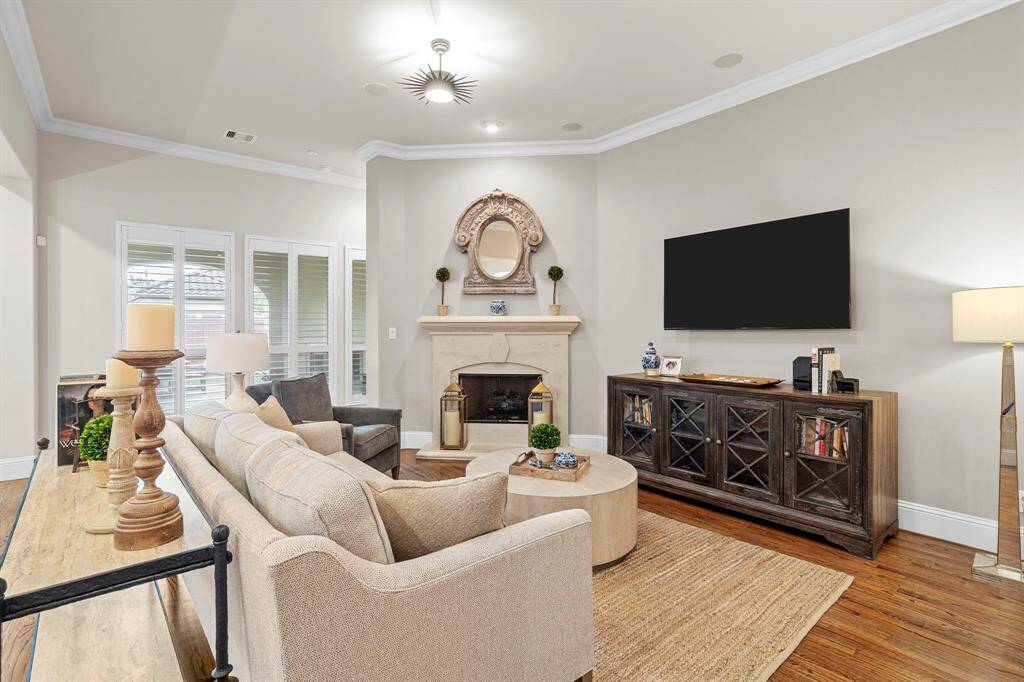 The living room features a striking cast stone fireplace nestled in the corner, a wall of windows with classic plantation shutters, and rich wood flooring that adds warmth and character to the space.