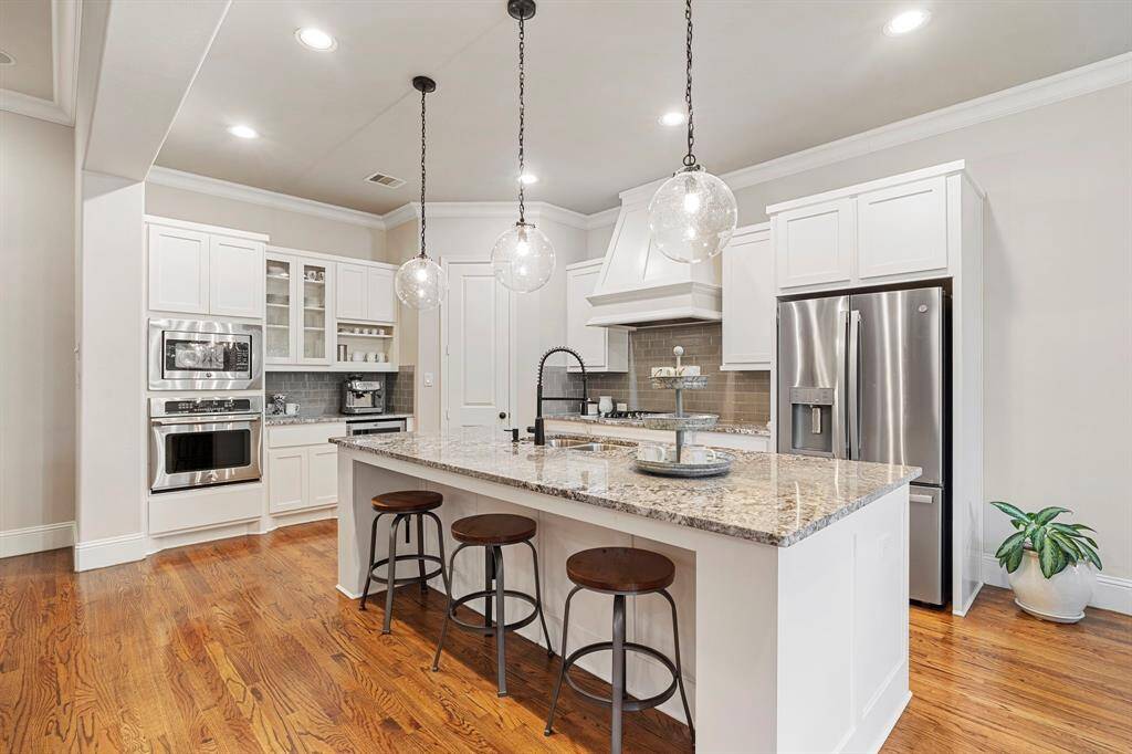 The bright and airy gourmet kitchen is a true showstopper— appointed with custom white cabinetry, a center island with breakfast bar, top-tier stainless steel appliances including a built-in wall oven & microwave, gas cooktop, built-in wine cooler, and so much more!