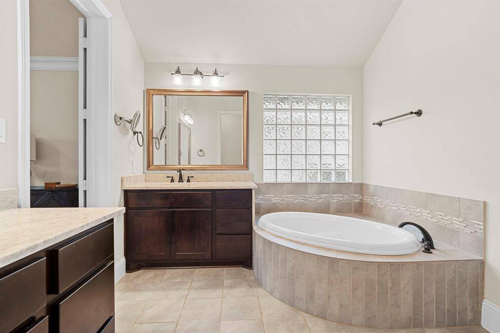 Indulge in this spa-inspired en suite bath, featuring a luxurious deep soaking tub, a walk-in shower with built-in bench, two vanities for added convenience, and a generously sized walk-in closet