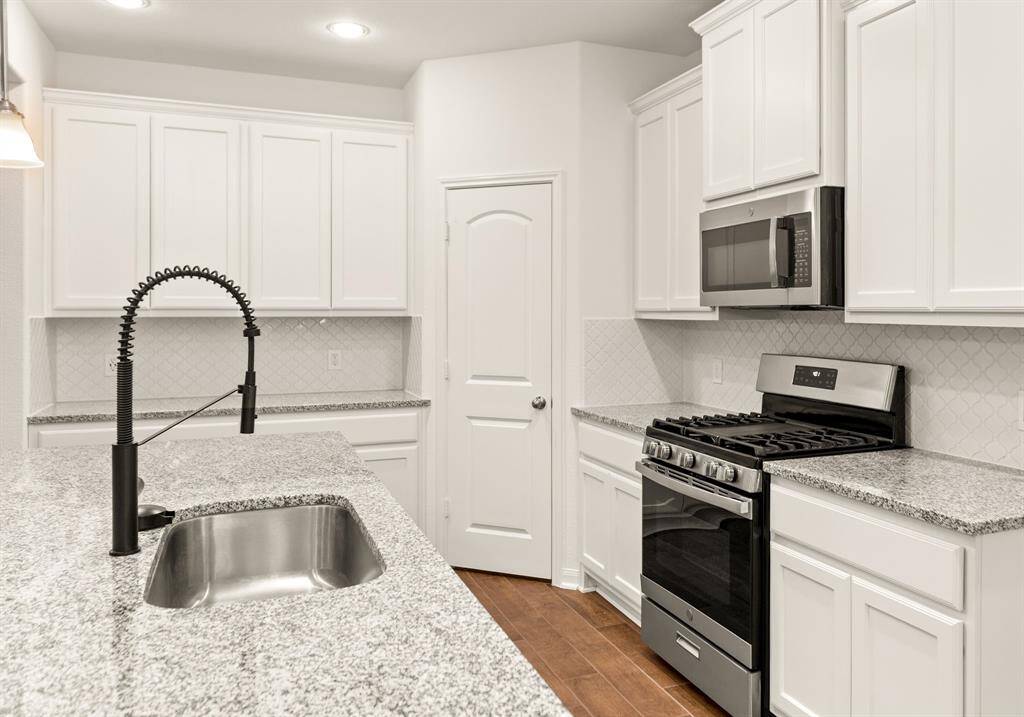 Modern kitchen with granite countertops, stainless steel appliances, and white cabinetry. Features a stylish black faucet and gas range, offering a sleek, contemporary look
