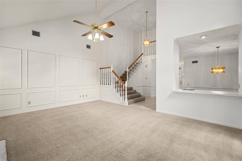 The spacious living room offers a welcoming atmosphere with a cozy fireplace, vaulted ceilings, and a wall of windows with plantation shutters. From this view, you’ll also spot the conveniently located wet bar—perfect for entertaining or relaxing evenings at home.