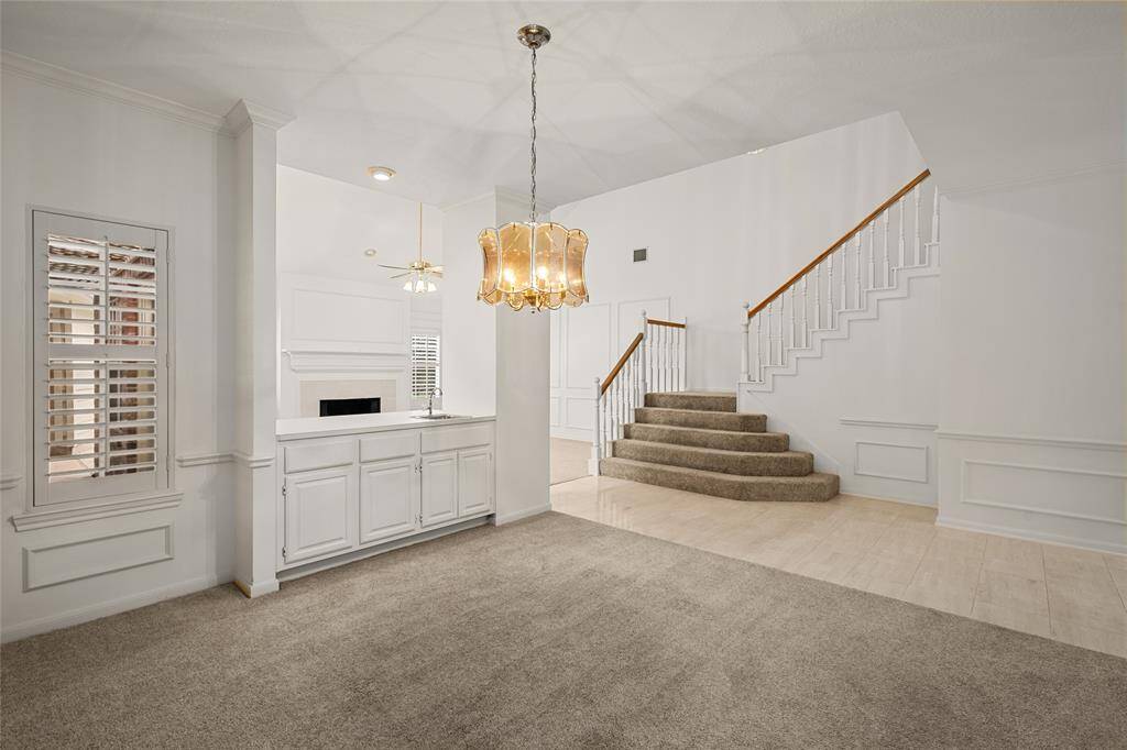 The formal dining area offers a bright and open layout with elegant wall molding, a statement chandelier, and easy access to both the living room and wet bar—making it perfect for entertaining. Neutral tones, plantation shutters, and sightlines to the grand staircase add to its classic appeal.