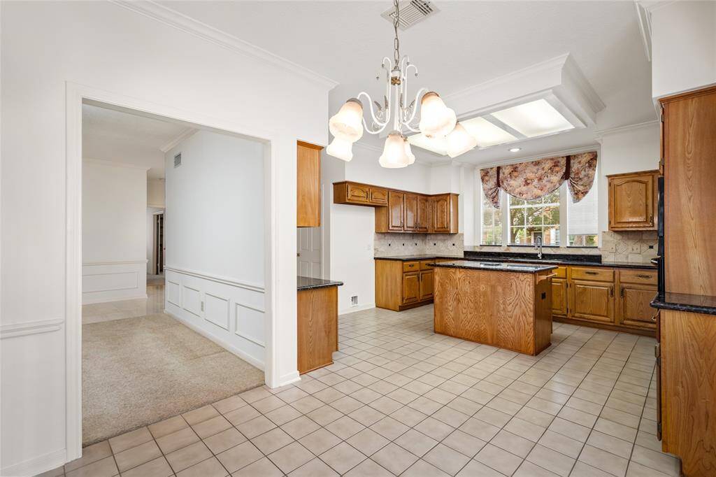 The seamless flow into the adjacent kitchen, featuring wood-paneled cabinets and a spacious center counter without a cooktop, ensures both functionality and style. With plenty of counter and cabinet space, this kitchen is ideal for meal preparation and offers an inviting atmosphere for cooking and conversation.